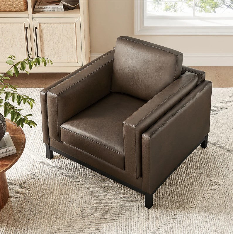 Amadeo Espresso Vegan Leather Modern Chair Brown leather armchair in a living room setting with a window and bookshelf in the background.