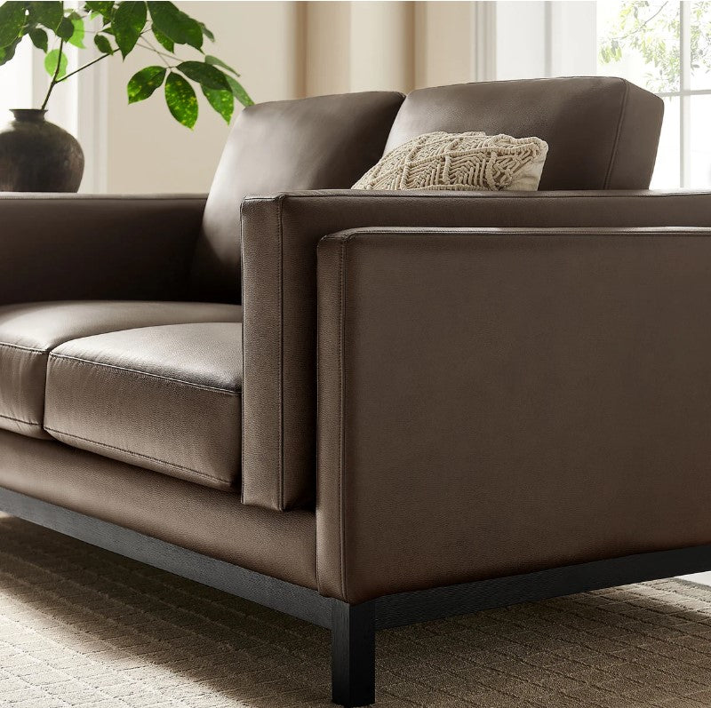 Amadeo Espresso Vegan Leather Modern Loveseat Brown leather sofa in a living room with a plant and window in the background