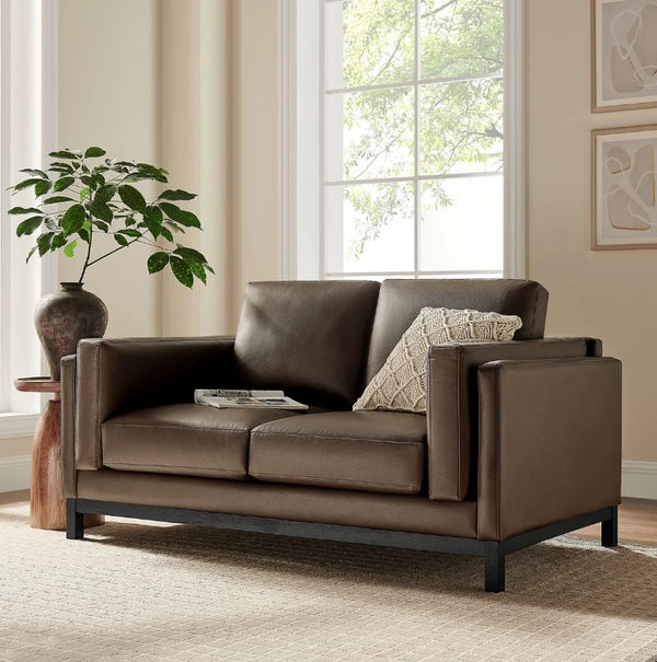 Amadeo Espresso Vegan Leather Modern Loveseat Brown leather sofa in a living room with a plant and window in the background