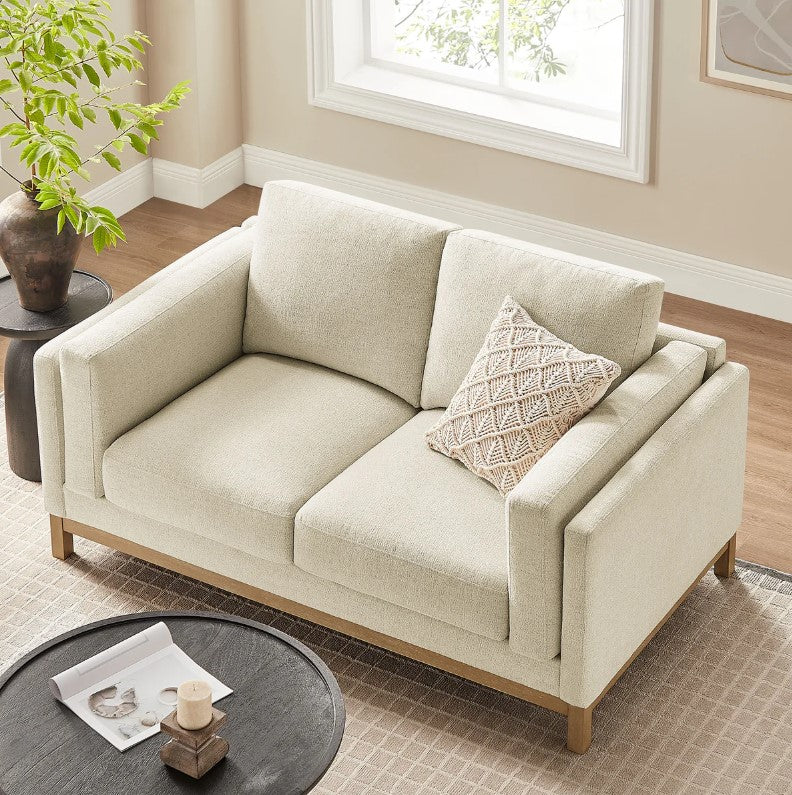 Amadeo Ivory Deep Seat Comfort Modern Fabric Loveseat Beige sofa in a living room with a plant and window in the background