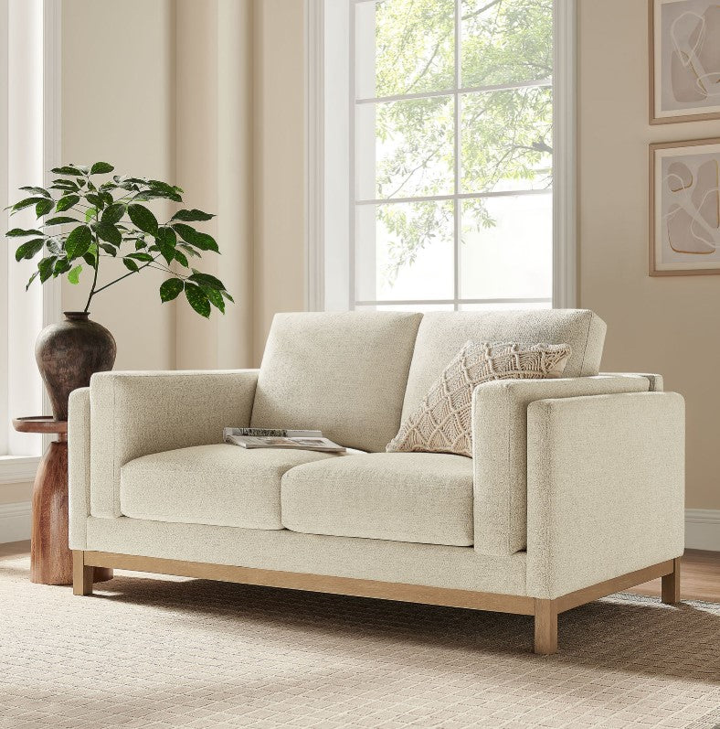 Amadeo Ivory Deep Seat Comfort Modern Fabric Loveseat Beige sofa in a living room with a plant and window in the background