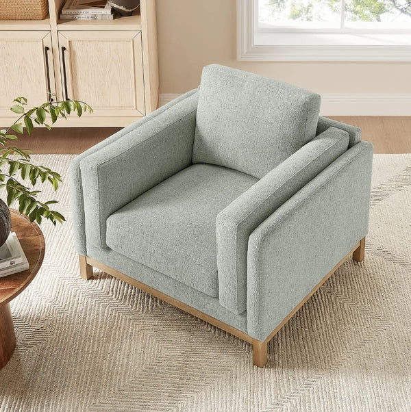 Amadeo Mist Deep Seat Comfort Modern Fabric Chair Gray armchair in a living room setting with a plant and wooden cabinet.