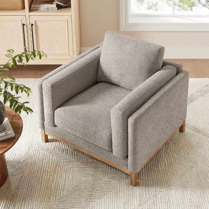 Amadeo Pewter Deep Seat Comfort Modern Fabric Chair Gray armchair in a living room setting with a window and shelves in the background.