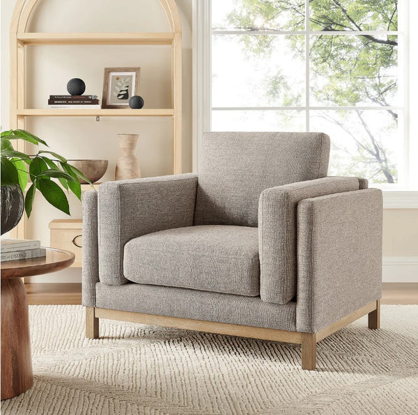 Amadeo Pewter Deep Seat Comfort Modern Fabric Chair Gray armchair in a living room setting with a window and shelves in the background.