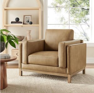 Amadeo Toast Vegan Leather Modern Chair Beige armchair in a living room setting with a bookshelf and window in the background.