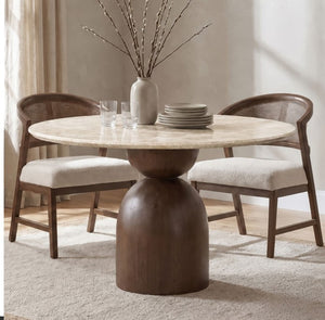 Artemos Contemporary Light Beige Round Dining Table Round dining table with a light beige stone top and a dark brown sculptural pedestal base, accompanied by two woven-back chairs with cream upholstered seats, shown in a softly lit dining room.
