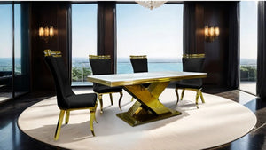 Asher Silver Black Leatherette Dining Chair 2-Pack A luxury dining set featuring a rectangular table with a white marble top and a gold metallic X-shaped base, surrounded by four black upholstered chairs with gold legs, set on a round white rug in a modern room with a view of the ocean.