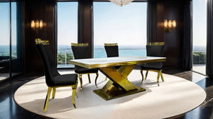 Asher Gold White Cross Shaped Glam Dining Table A luxury dining set featuring a rectangular table with a white marble top and a gold-finished geometric pedestal base, surrounded by four black upholstered chairs with gold trim, set on a round white rug in a modern room with a sea view.