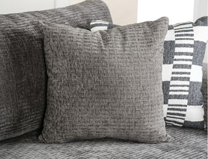 Assia L-Shape Sectional Sofa Gray textured pillows on a sofa with a striped pillow in the background