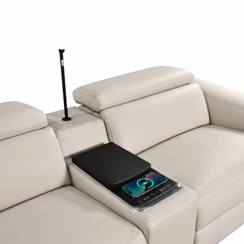 Aurelia Beige Modern Air Leather Sectional Sofa Powered Recliner A cream-colored leather sectional sofa with a center armrest console holding a black tablet and a smartphone on a charging pad, with a black floor lamp standing in the armrest compartment.
