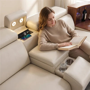 Aurelia Beige Modern Air Leather Sectional Sofa Powered Recliner  woman relaxes in a cream-colored leather reclining sofa, reading a book. The sofa features integrated cup holders, a side table with wine glasses, and a headrest with built-in lights.