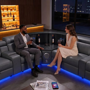 Aurelia Modern Air Leather Sectional Sofa Powered Recliner A man in a gray suit and a woman in a cream dress sitting on a curved dark gray leather barsofa, holding wine glasses in a modern home bar setting with blue under-glow.