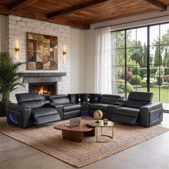 Aurelia Modern Air Leather Sectional Sofa Powered Recliner A large black leather reclining sectional sofa with built-in media console and side lighting, staged in a modern living room with a fireplace, stone wall, large windows, and outdoor greenery visible.