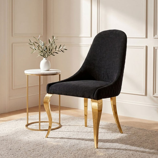 Betsy Black Upholstered Modern Chair (2/CTN) A modern dining chair upholstered in black velvet with curved gold metal legs, styled in a bright room next to a small marble-top side table.