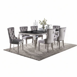 Betsy Silver Black Glass Top Modern Dining Room Table A 7-piece dining set featuring a rectangular glass-top table with a polished silver frame and six matching tufted gray velvet chairs, styled on a shag rug in a modern dining room.