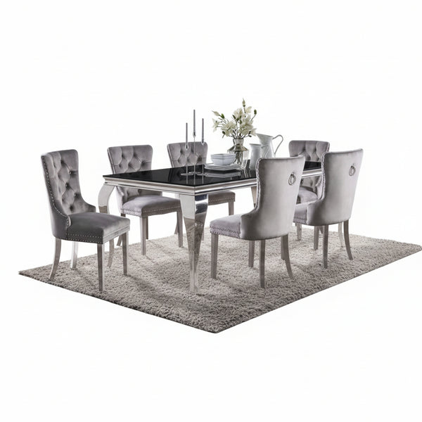 Betsy Silver Black Glass Top Modern Dining Room Table A 7-piece dining set featuring a rectangular glass-top table with a polished silver frame and six matching tufted gray velvet chairs, styled on a shag rug in a modern dining room.