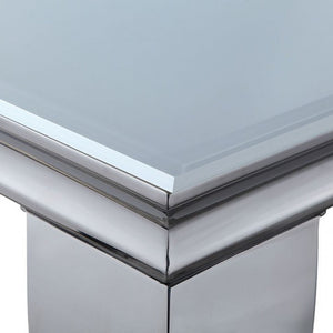 Betsy Silver White Glass Top Modern Dining Room Table Close-up of a polished metallic table corner with a smooth reflective silver base and a pale blue-gray top surface.