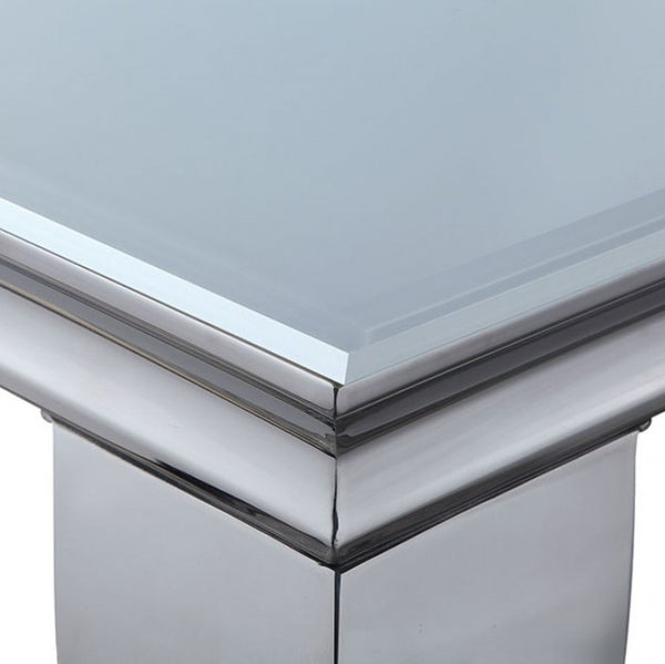 Betsy Silver White Glass Top Modern Dining Room Table Close-up of a polished metallic table corner with a smooth reflective silver base and a pale blue-gray top surface.