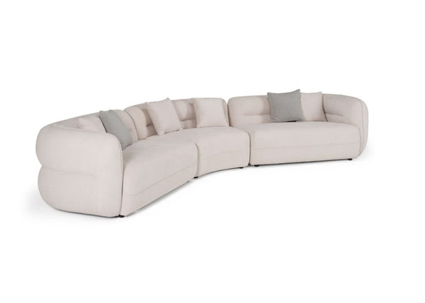 Boniser Modern Curved Off White Sectional Sofa A curved modular upholstered sofa in a light warm beige fabric, accented with several square throw pillows in light gray and cream, shown on a plain white background.