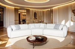 Boniser Modern Curved Off White Sectional Sofa A luxurious white curved modular sofa in a grand, elegant room with warm gold and cream lighting, a round wooden coffee table, and a beige rug.