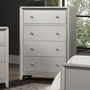 Borch Contemporary Champagne Finish Chest A light gray four-drawer dresser with round silver knobs, positioned in a bedroom setting next to a bed and another matching piece of furniture.