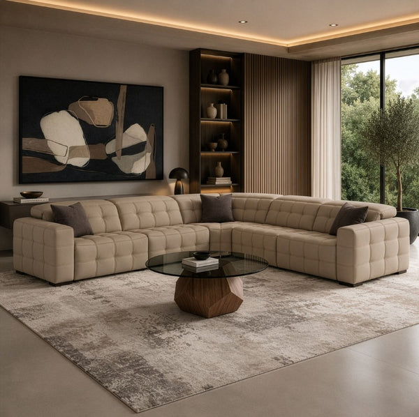 Carney 3 Recliners Beige Leather Modern Sectional Sofa A modern tufted beige sectional sofa arranged in an L-shape in a stylishly decorated living room with a glass-top coffee table, textured rug, shelving, and large windows.