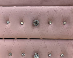 A close-up of dusty pink velvet upholstery with diamond tufting and clear faceted crystal buttons.
