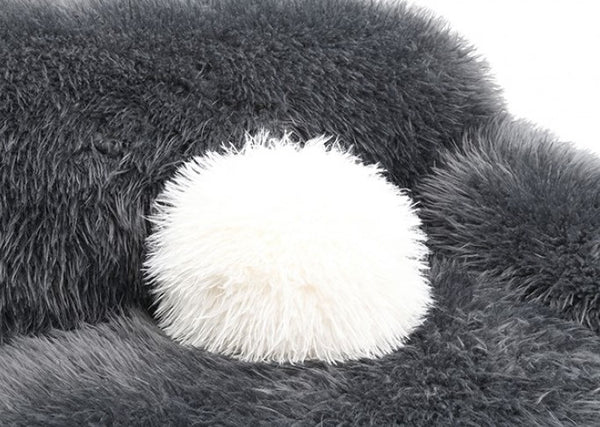 Dareen Contemporary Gray Faux Fur Sofa with Ball Pillows Close-up of a fluffy gray pillow with a white pom-pom on a white background