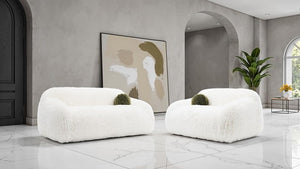 Dareen Contemporary White Faux Fur Sofa with Ball Pillows Two white armchairs in a modern room with abstract art and plants.