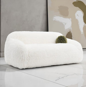 Dareen Contemporary White Faux Fur Sofa with Ball Pillows White fluffy chair with a green cushion in a modern room.