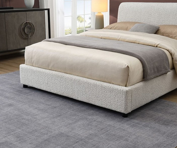 Doira Modern  Style Upholstered Bed White Finish Bedroom with a bed featuring beige and gray bedding, a lamp, and a sideboard.