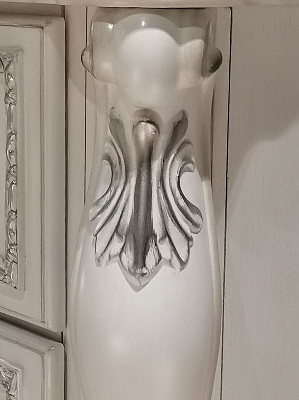 Dresden Bone White Traditional Style Nightstand vA white decorative wall sconce with a sculpted, winged or acanthus leaf-like relief design on the front, mounted on a white paneled cabinet or wall.