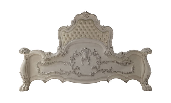 Dresden Bone White Traditional Silhouette Upholstered Bed An ornate, vintage-style upholstered headboard in a distressed off-white or cream color, featuring intricate carved floral details and a tufted button pattern on the top panel.