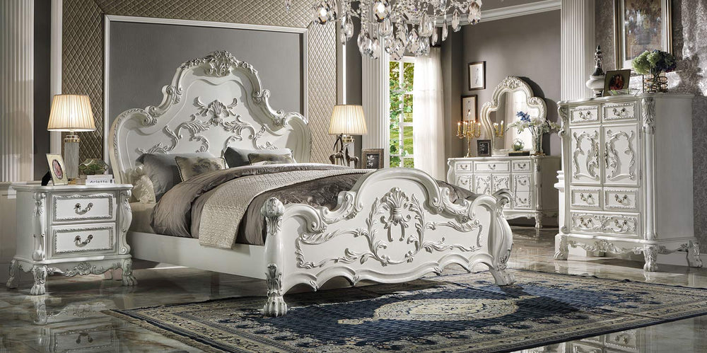 Dresden Bone White Traditional Silhouette Leaf Carving Inlay Bed An ornate white carved bedroom furniture set in a luxury bedroom, featuring a bed with a high sculpted headboard and footboard, a matching nightstand, dresser, and mirror, all styled with gray and beige bedding and a blue patterned rug.