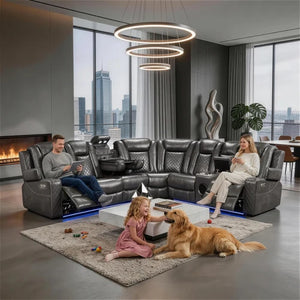 Eloise Power Gray Recliner Sectional Sofa LED Multi Color Lights A large black leather sectional sofa with recliners is shown in a modern living room with a man, woman, and dog interacting on a rug in front of it. The room has large windows with a city skyline view, a hanging ring chandelier, and a fireplace.