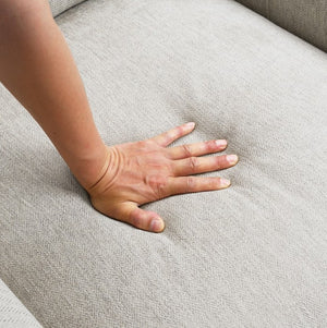 Estrella Light Taupe Brown Slope Flair Arm Chair A close-up of a person's hand pressing down on a light gray textured fabric sofa cushion to show its texture and comfort.