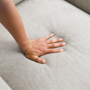 Estrella Light Taupe Brown Slope Flair Arm Sofa A close-up of a person's hand pressing down on a light gray textured fabric sofa cushion to show its texture and comfort.