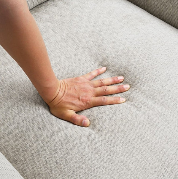 Estrella Light Taupe Brown Slope Flair Arm Sofa A close-up of a person's hand pressing down on a light gray textured fabric sofa cushion to show its texture and comfort.