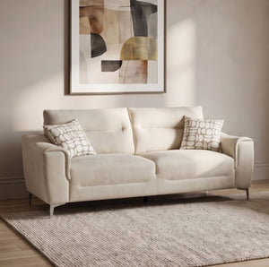 Estrella Light Taupe Brown Slope Flair Arm Sofa An off-white upholstered loveseat with two patterned throw pillows, styled in a living room setting on a textured rug with a framed abstract print on the wall behind it.