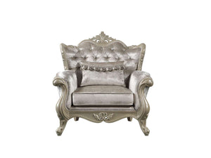 Ethaan Button Tufted Traditional Fabric Chair A single ornate baroque-style armchair upholstered in shimmering champagne-gray velvet, featuring a tufted backrest, decorative carved frame, and a matching fringed accent pillow, shown against a plain white background.