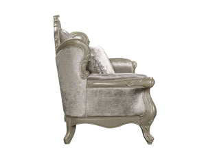 An ornate vintage-style armchair upholstered in textured champagne-colored velvet with carved silver-painted wooden frame details, shown from a three-quarter angle against a plain white background.
