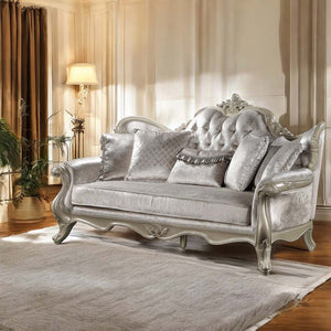 Ethaan Button Tufted Traditional Fabric Sofa A luxurious silver velvet loveseat sofa with ornate carved silver-painted wooden arms and legs, styled in a warm, elegant living room with beige curtains, a floor lamp, and a plush rug.