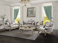Ethaan Button Tufted Traditional Fabric Sofa A luxury French-style living room furniture set featuring a tufted sofa, two matching armchairs, and a carved coffee table, all in a silver and gray fabric with ornate silver frames, arranged on a gray rug in a grand room with green curtains.