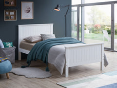 Gallow White Finish Twin Bed A white wooden single bed frame with a slatted headboard and footboard, styled in a modern bedroom with gray and teal bedding, a floor lamp, and a window looking out to a garden.