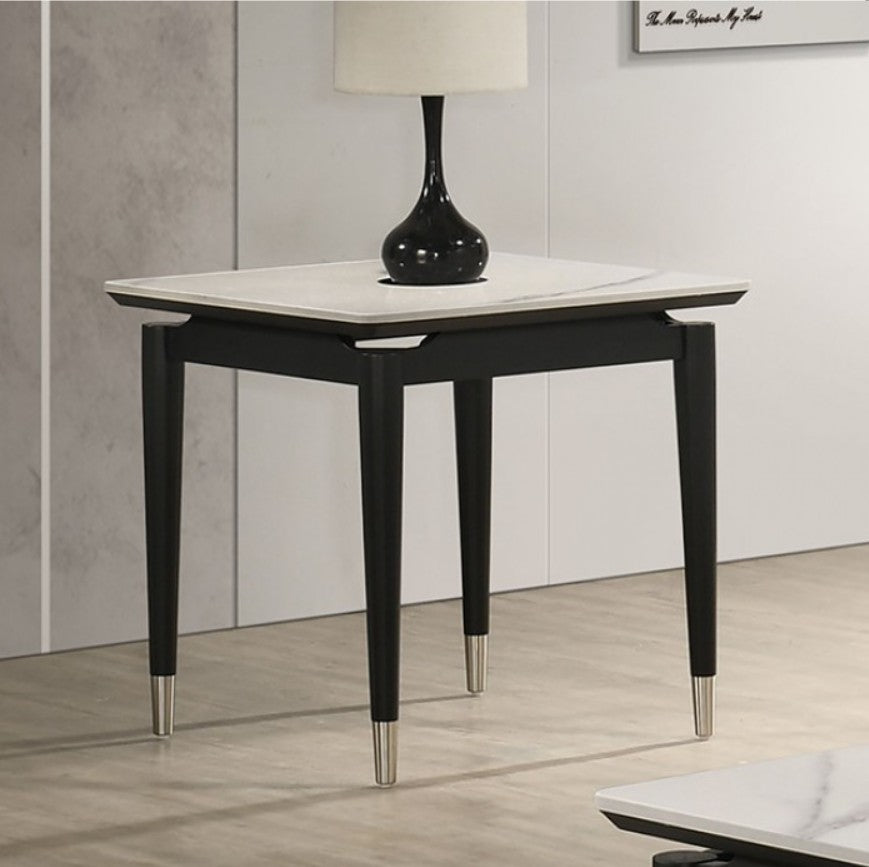 Grayson Contemporary Black White Sintered Stone Top End Table A modern black wooden side table with a white marble top and silver metal feet, styled with a black lamp in a minimalist room setting.