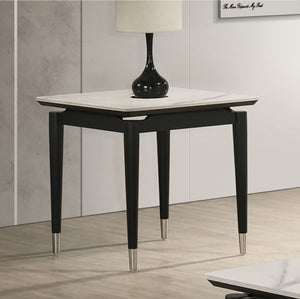 Grayson Contemporary Black White Sintered Stone Top End Table A modern black wooden side table with a white marble top and silver metal feet, styled with a black lamp in a minimalist room setting.