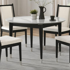 Grayson Contemporary Black White Sintered Stone Top Round Dining Table A round dining table with a white marble-look top and black legs, surrounded by five matching chairs with cream upholstered seats and black frames, set on a light gray rug in a bright dining room.