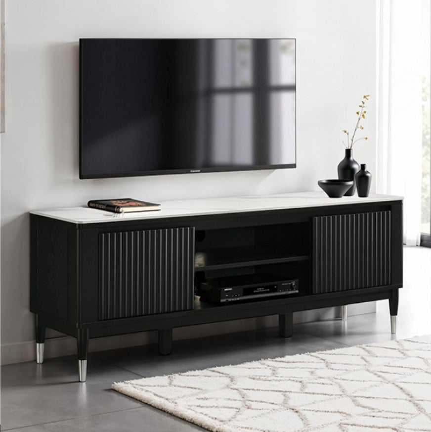 Grayson Contemporary Black White Sintered Stone Top TV Console A modern black TV stand with a white marble-look top and silver metal legs, shown in a styled living room setting with a wall-mounted TV, decorative vases, and a patterned rug.