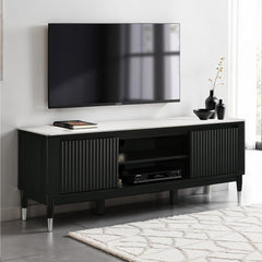 Grayson Contemporary Black White Sintered Stone Top TV Console A modern black TV stand with a white marble-look top and silver metal legs, shown in a styled living room setting with a wall-mounted TV, decorative vases, and a patterned rug.