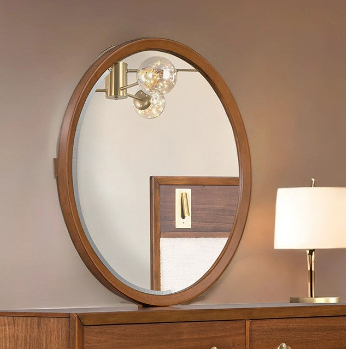 Hermin Modern Style Walnut Mirror Round wooden mirror on a dresser with a lamp in the background